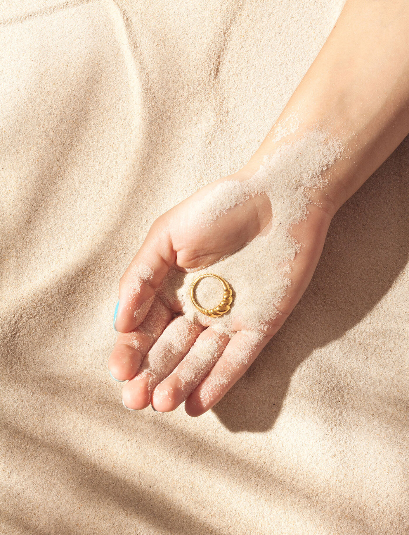 Auric Jewels — gold ring resting in a hand cradled by warm sand
