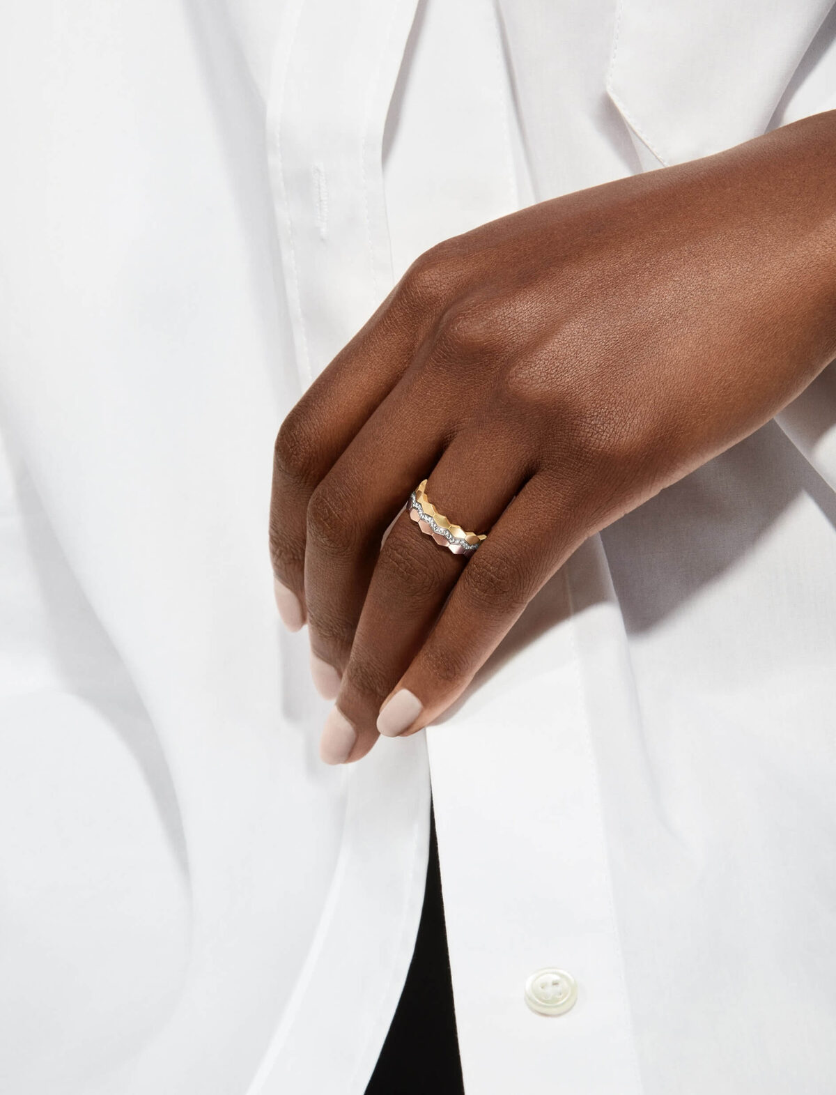 Sculptural gold and diamond band on a hand against a white shirt