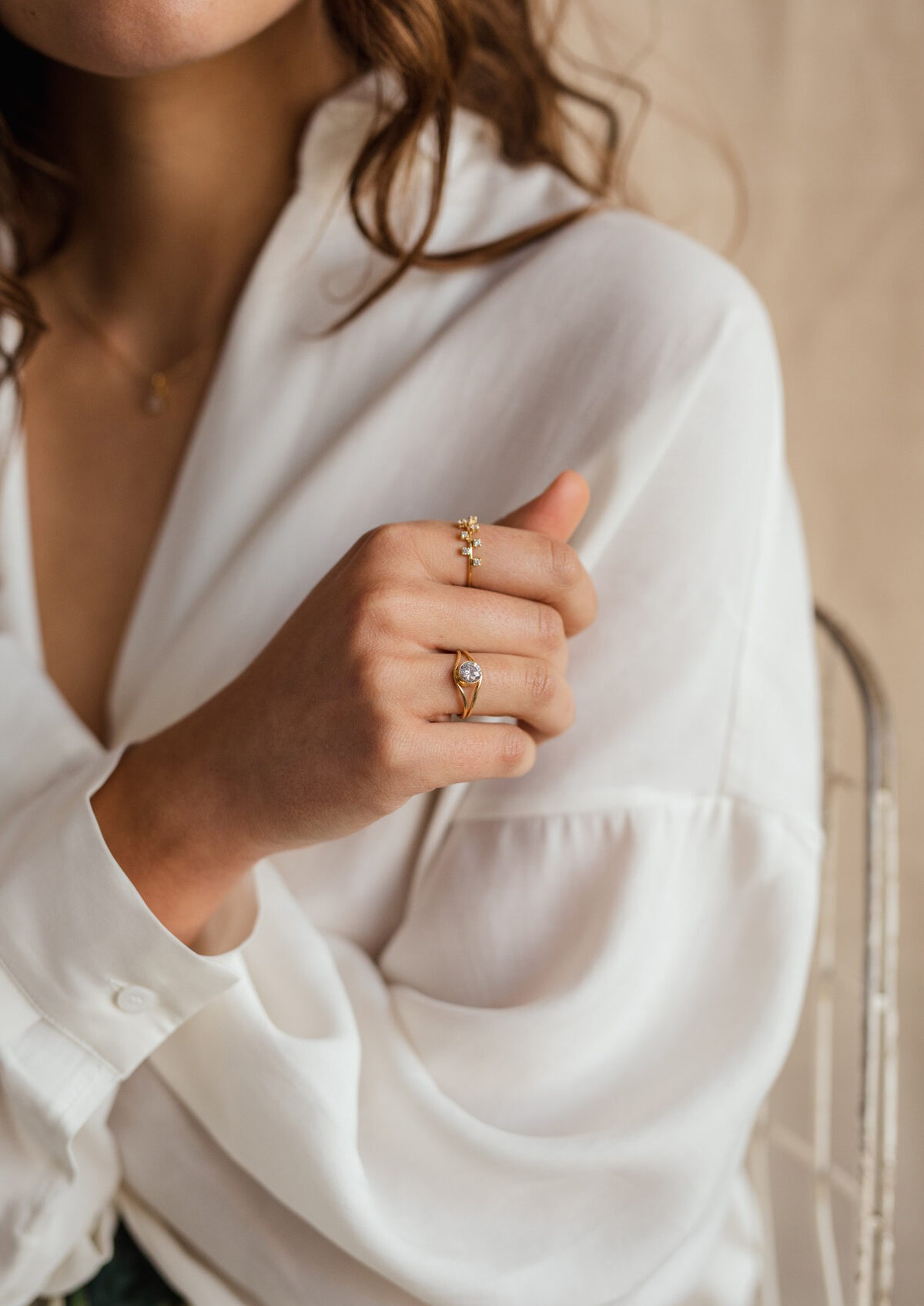 Stacked fine gold and diamond rings on a hand against a soft white blouse