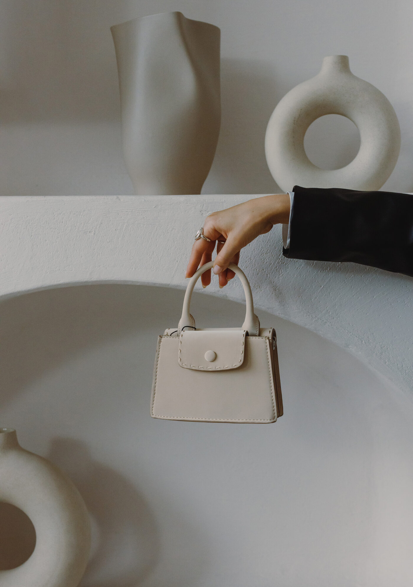 Cream leather mini bag held against ceramic vases — Sasstain product