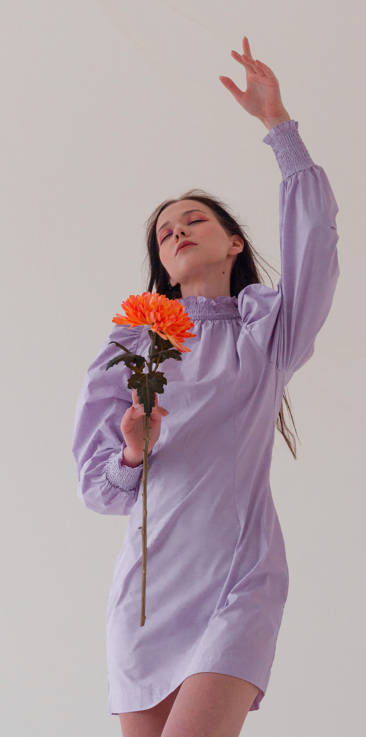 Model in lavender shirt dress holding a chrysanthemum, lifted arm